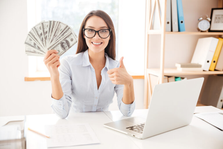 Businesswoman holding money while making thumbs up gesture