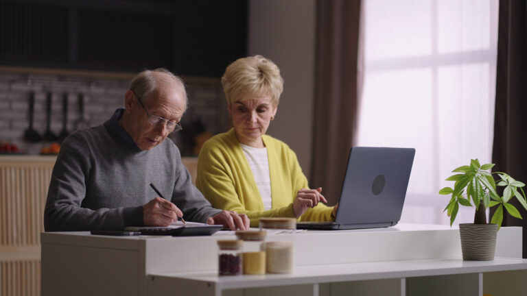 Elderly couple reviewing Social Security statement with calculator, discussing tax strategies